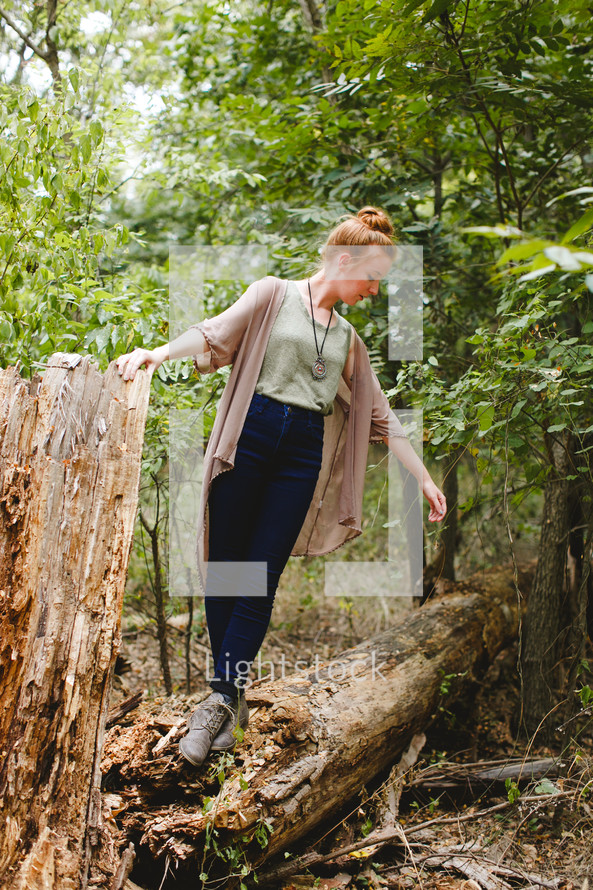 woman standing on a fallen tree in a forest alone 