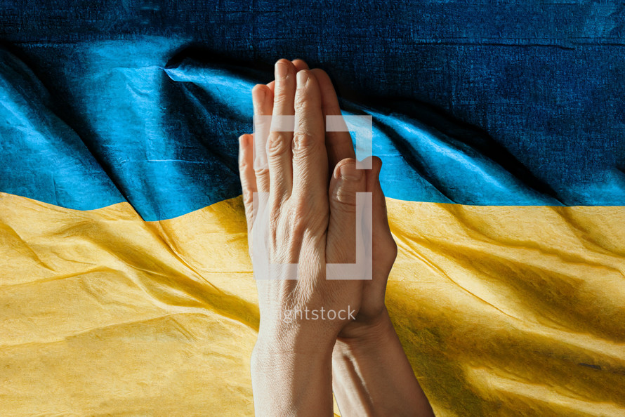 Pray for Ukraine. Hands in pray against ukrainian flag. Copy space