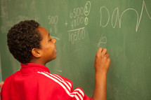 child writing on a classroom chalkboard 