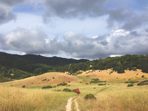 A jogger on a path through a grassy field surrounded by hills.