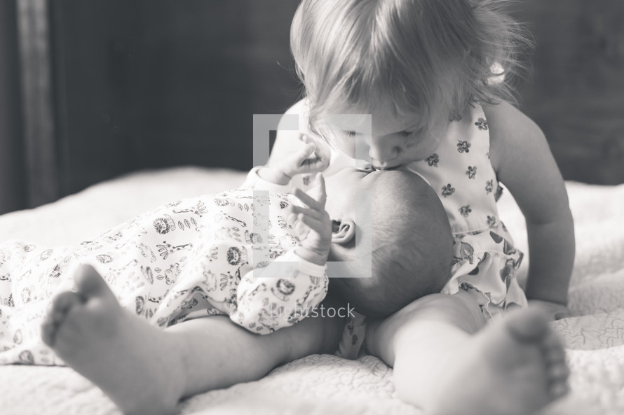 a toddler girl kissing her baby sister 