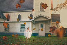 girl in a dress playing in fall leaves in front of a church 