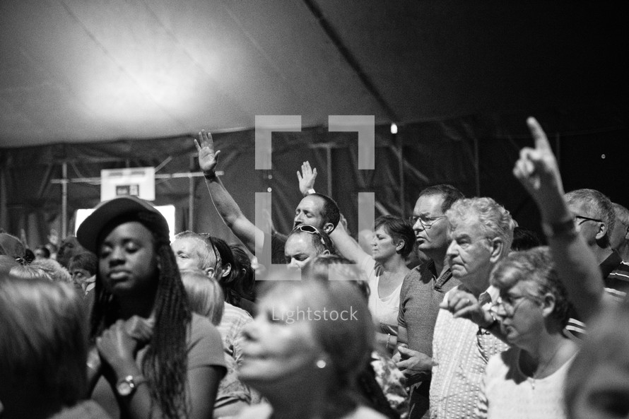 A diverse group of people standing and worshipping together in a large tent.
