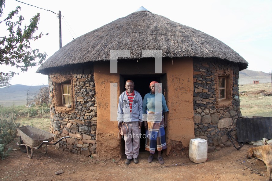 husband and wife standing in front of their modest house in a village 