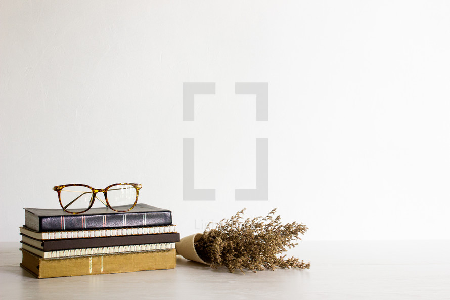 Study concept with reading glasses and flowers on wooden white table with natural light. 