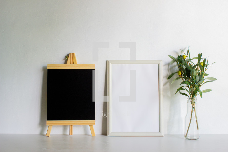 vase of olive branches and blank frame and easel 