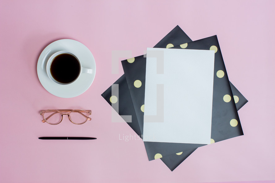 paper, coffee cup, and reading glasses on pink background 