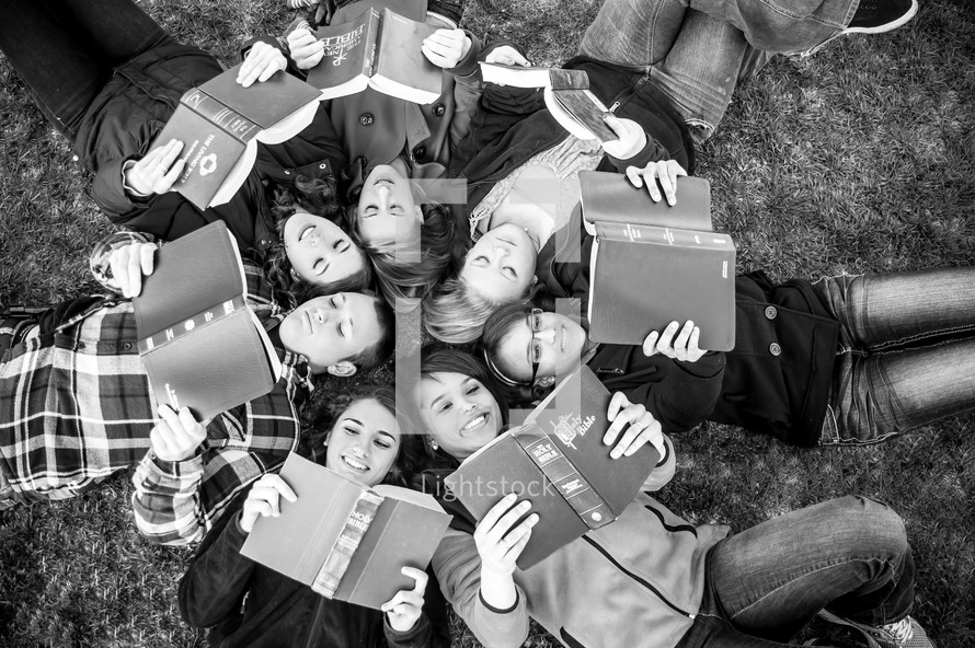 teens in a youth group lying in the grass reading Bibles