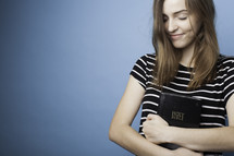 a teen girl hugging a Bible 