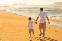 a father and son walking on a beach 