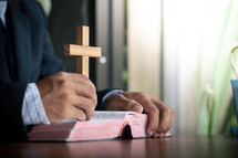 a man holding a wood cross reading a Bible 