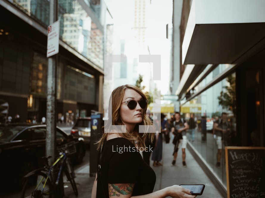 A woman holding a cell phone looks back over her shoulder while on a busy city street.