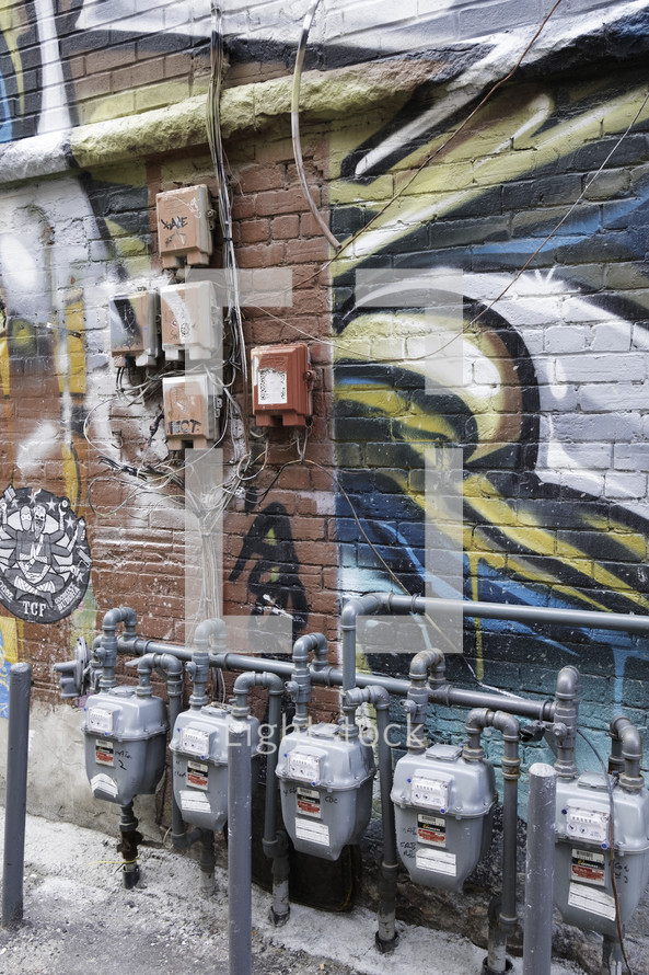 utility boxes and gas meters and graffiti on a wall 