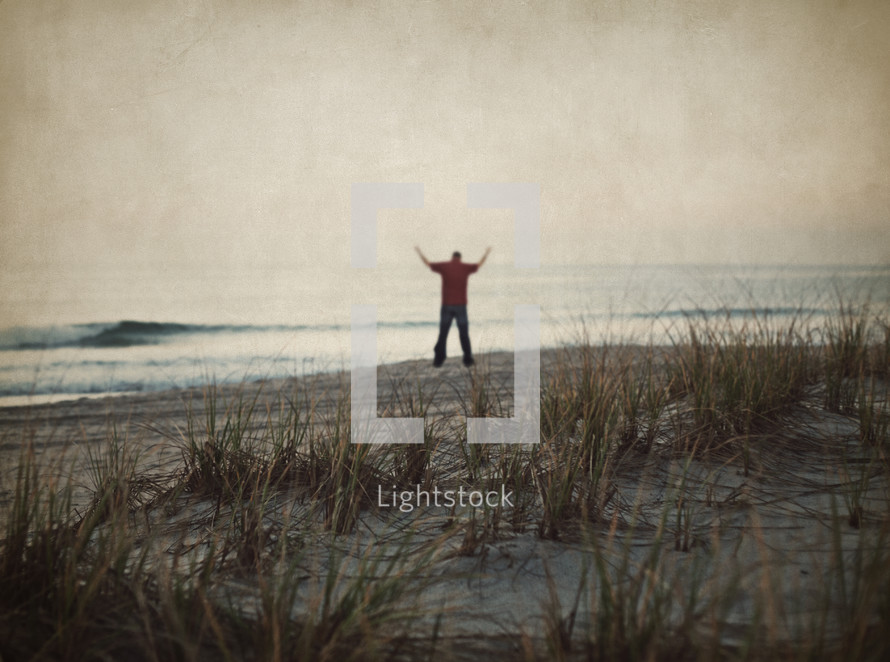 man standing on a beach with his hands raised in praise and worship to the lord