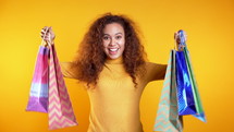 Happy young woman with colorful paper bags after shopping isolated on yellow studio background. Seasonal sale, purchases, spending money on gifts concept.