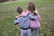 A young boy and girl walking with their arms around each other.