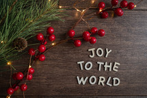 red berries and fairy lights on a wood background and words Joy to the world 