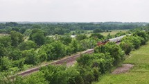 Freight train coming in creates a parallax effect with trees and the countryside. 