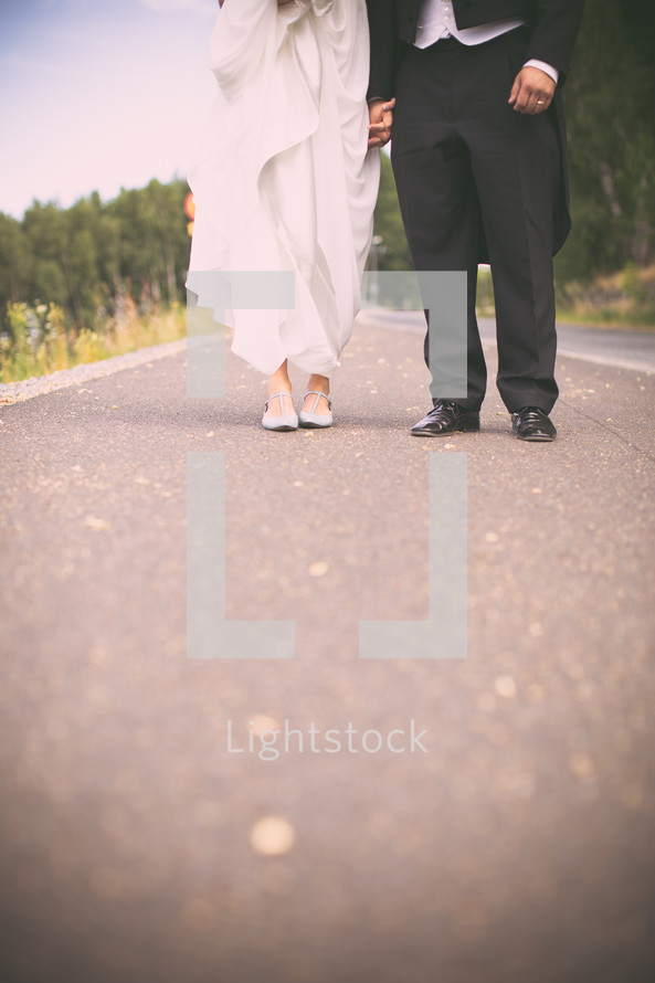 torso and legs of bride and groom standing on asphalt 