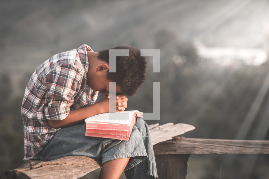 a boy praying outdoors over a Bible 