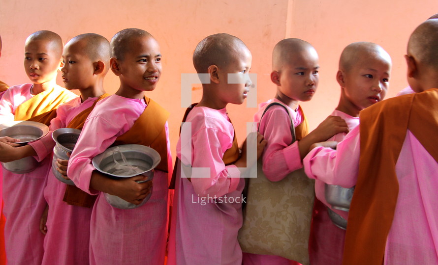 Buddhist novice monks in traditional pink dress carrying begging bowls