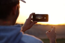 a man taking a picture of the sunset with his cellphone 