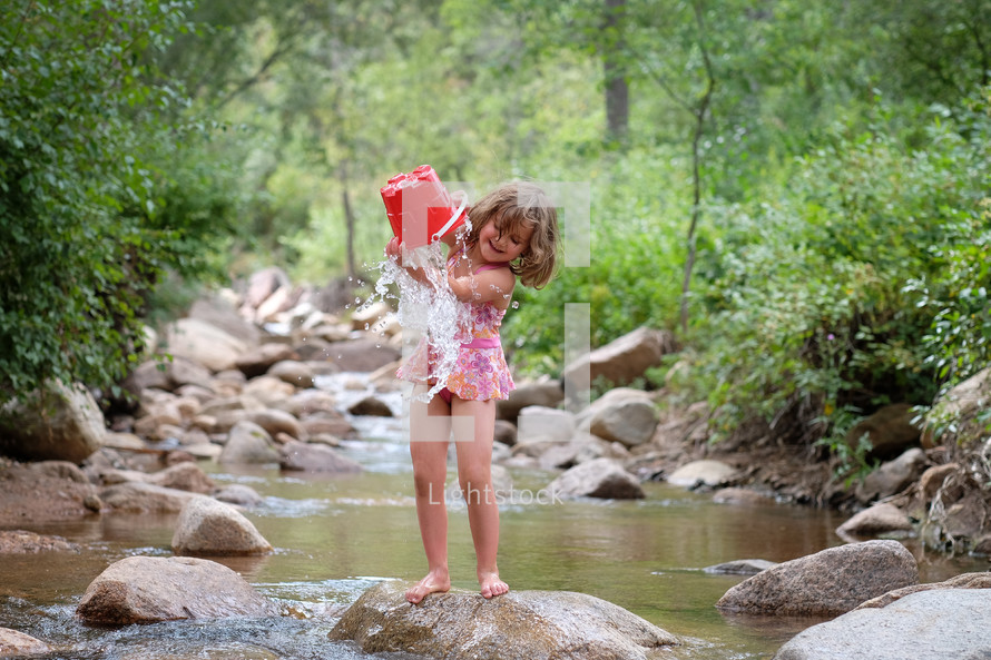 a girl child playing with a bucket of water in a stream 