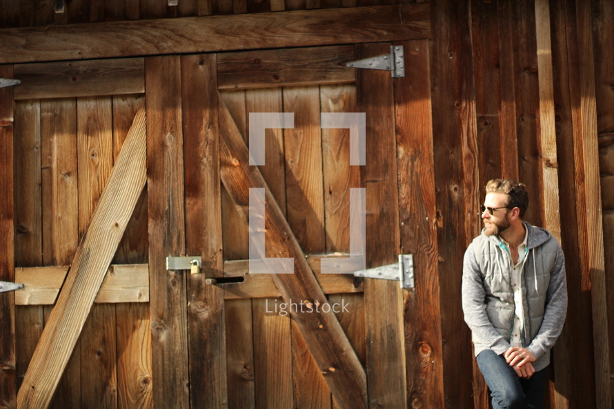 a bearded man standing by barn doors 