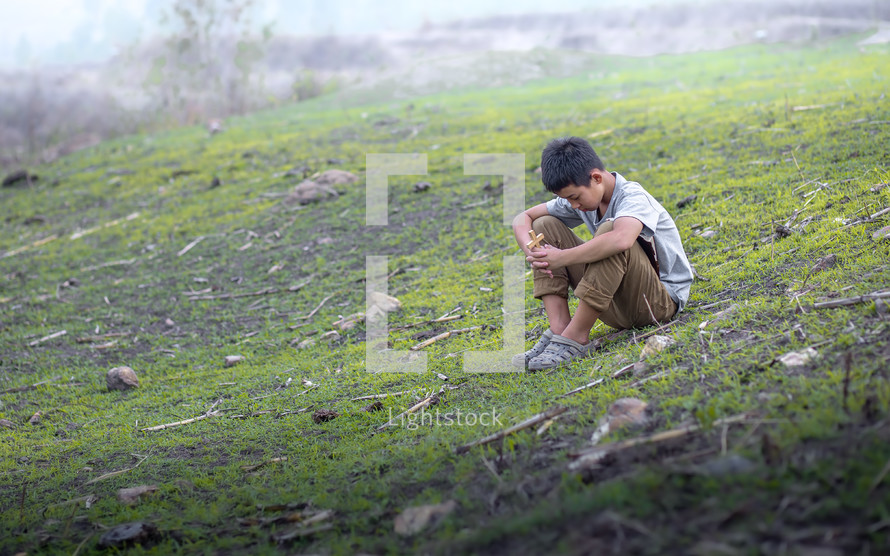 a little boy sitting on a hill praying 