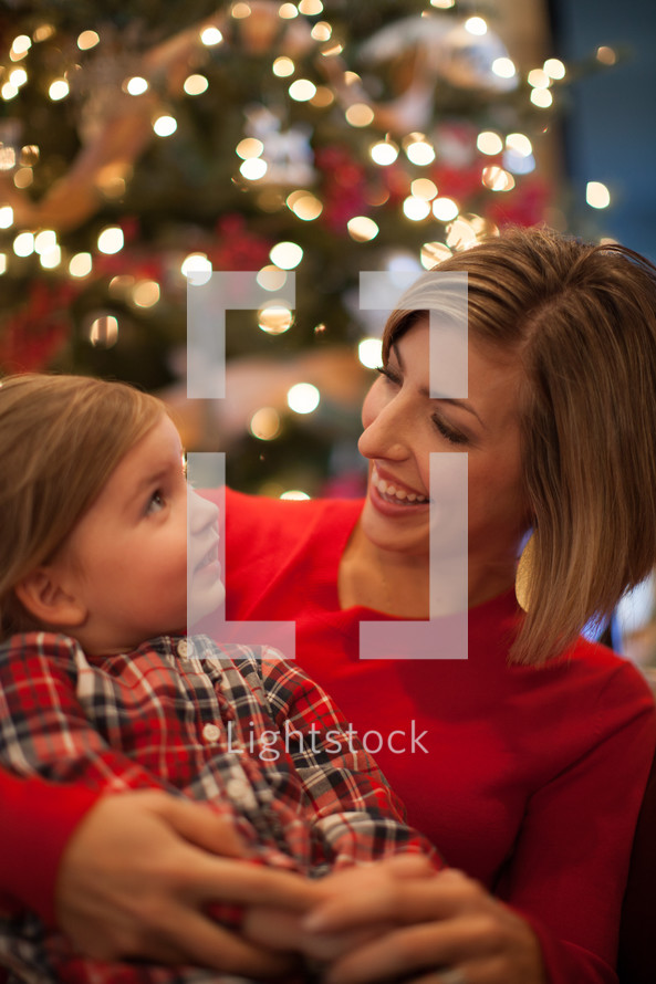 mother and daughter snuggling in front of a Christmas tree 