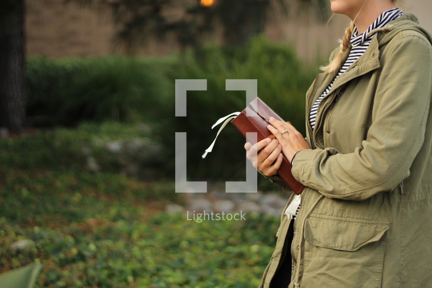 a young woman holding a Bible outdoors 