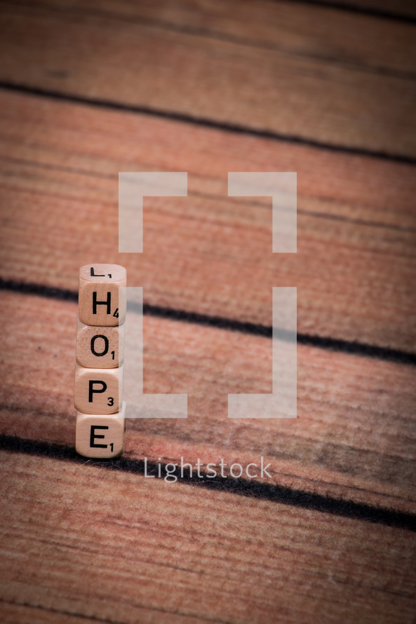 A stack of dice, spelling "hope," on a wooden table.