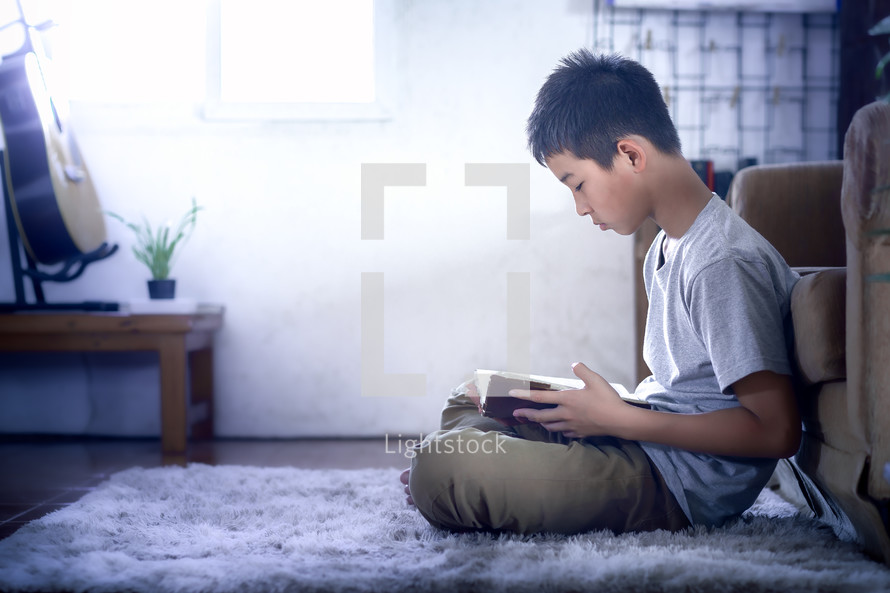 a boy sitting on a rug reading a Bible 