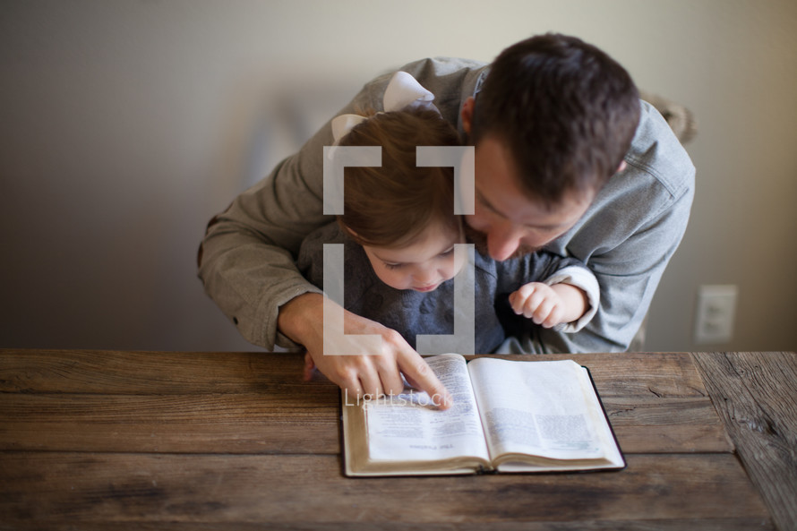 father and toddler daughter reading a Bible together 