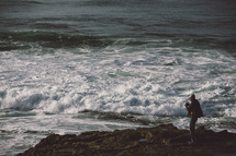man taking pictures from a rocky shore of the swirling, stormy waves