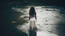 Baptism. Beautiful girl in a long white dress standing in the river.