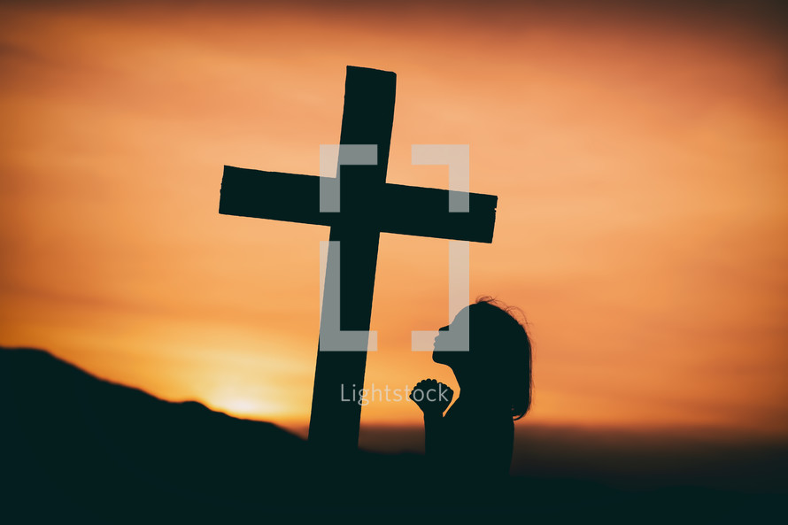 girl praying near a cross at sunset 