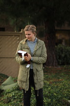 a young woman in a coat holding a Bible outdoors 