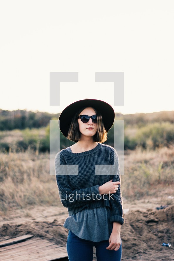 a woman in a sun hat and sunglasses standing outdoors 