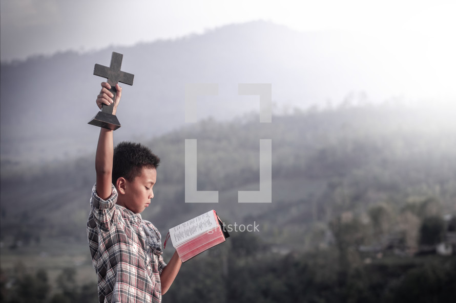 a boy holding a cross and Bible outdoors 