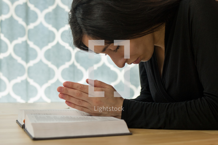 a woman praying over the pages of a Bible 
