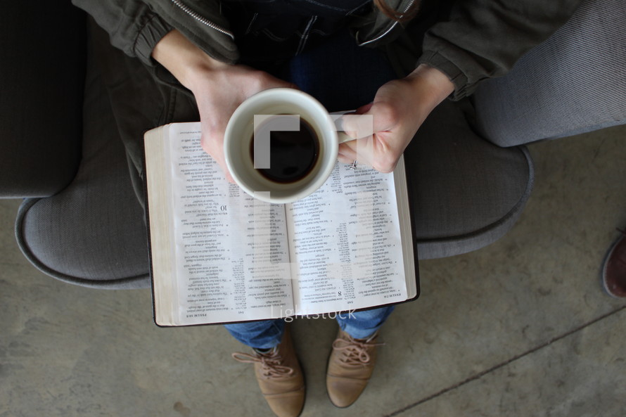 a woman reading a Bible in her lap while holding a coffee mug 