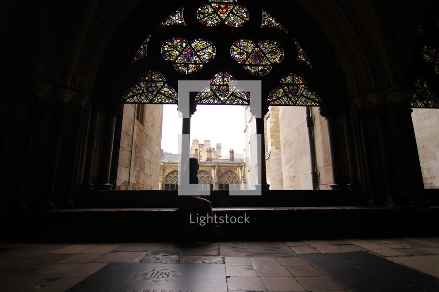 woman sitting under stained glass windows looking out through a window 