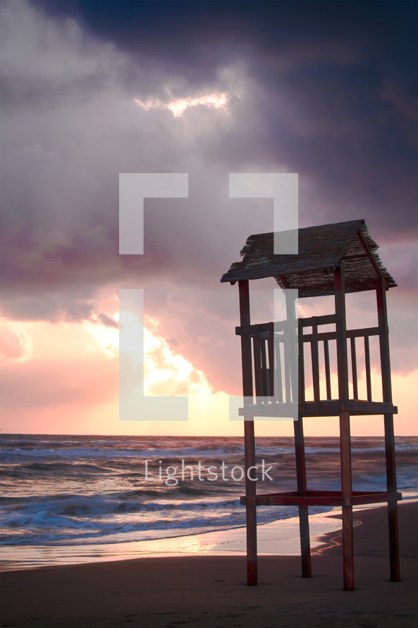 Landscape of beach with rough sea and the wooden lookout tower at sunset.