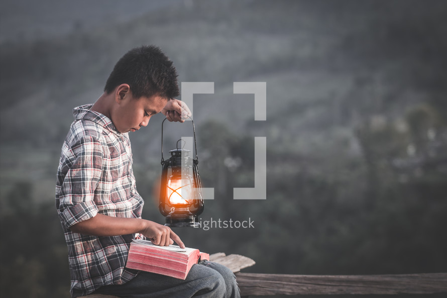 a child holding a lantern and reading a Bible outdoors 