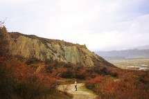 a woman walking on a dirt path surrounded by cliffs 