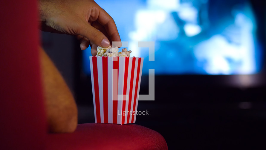 a man reaching for popcorn while watching a movie 