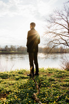 a man looking out at the water standing on a lake shore 