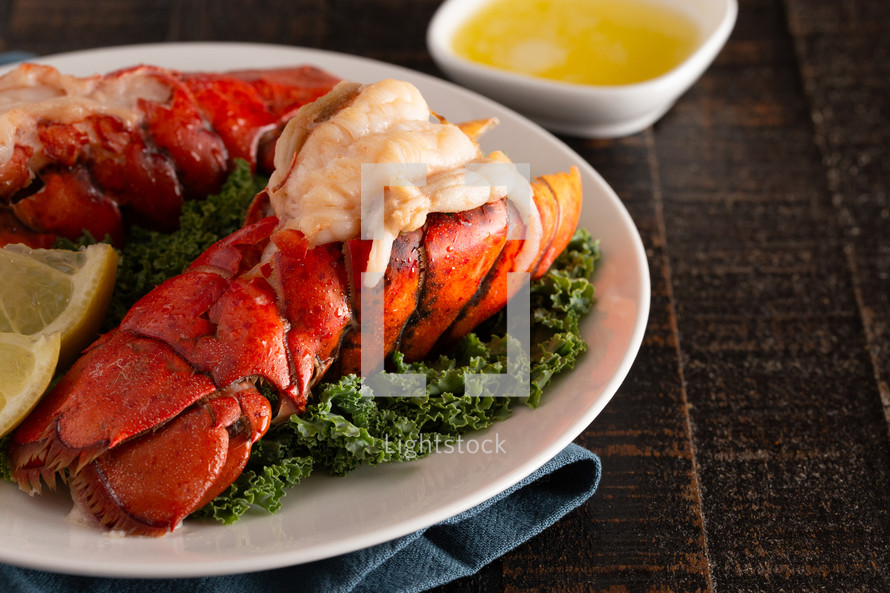 two Broiled Lobster Tails on a Bed of Kale with Lemon Slices