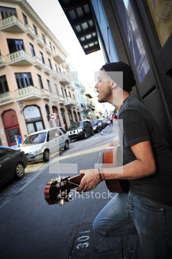 Man playing guitar and singing on sidewalk.